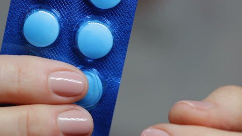 Female hands take out pill out of blue blister and woman intently looks and eats