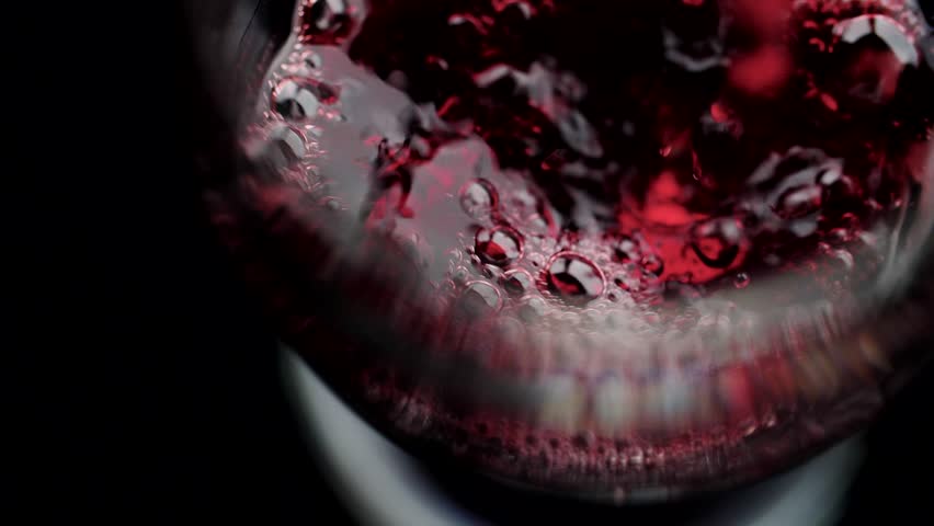 Red wine pouring in to a glass, slow motion on white background