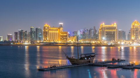 View from Katara Beach day to night transition timelapse after sunset in Doha, Qatar, towards the West Bay and city center. Illuminated skyscrapers. Old ship on foreground