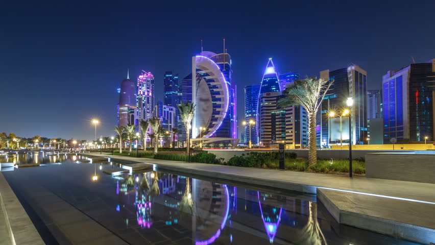 The skyline of Doha by night with starry sky seen from Park timelapse hyperlapse, Qatar. Illuminated skyscrapers and towers reflected in water of fountain