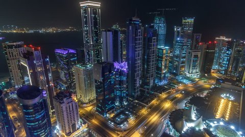 The skyline of the West Bay area from top in Doha timelapse, Qatar. Illuminated modern skyscrapers aerial view from rooftop at night. Traffic on the road