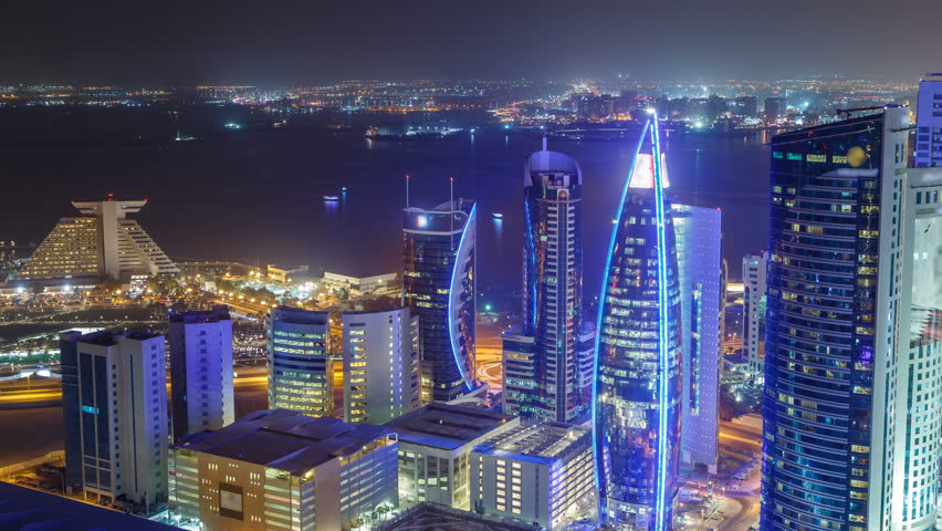 The skyline of the West Bay area from top in Doha timelapse, Qatar. Illuminated modern skyscrapers aerial view from rooftop at night. Gulf on background and traffic on the road