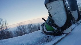 Feet of active guy masterfully snowboarding from high hill in snowy mountains