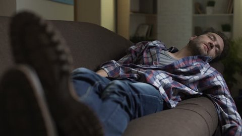 Drunken man sleeping on couch, scratching belly in his sleep, after night out