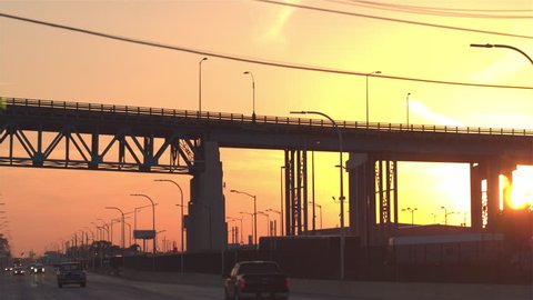 CLOSE UP: Freight container semi trucks driving from the distribution center storage depot to the busy multiple lane highway over a overpass bridge transporting goods at gorgeous golden light twilight