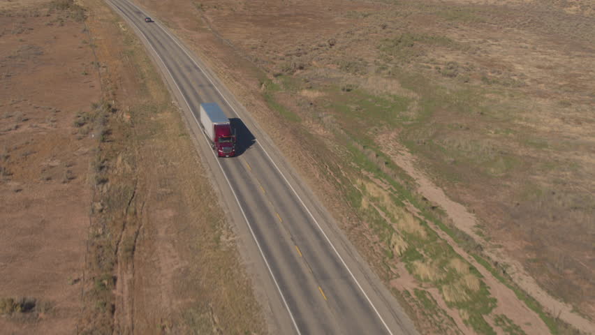 AERIAL CLOSE UP: Unbranded white semi truck driving on empty road, transporting goods on sunny day. Freight container truck hauling and delivering cargo across a country. Trucking logistics shipping Royalty-Free Stock Footage #1007447290