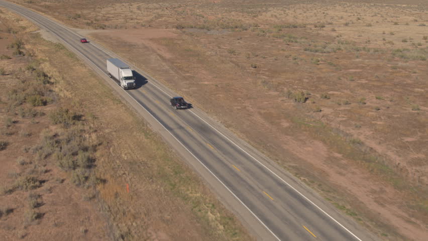 AERIAL CLOSE UP: Unbranded white semi truck driving on empty road, transporting goods on sunny day. Freight container truck hauling and delivering cargo across a country. Trucking logistics shipping Royalty-Free Stock Footage #1007447299