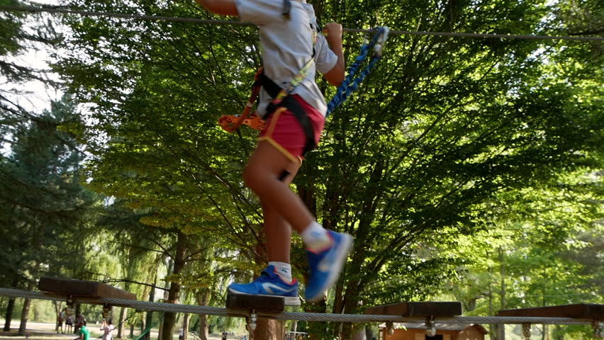 Boy walks on rope bridge in adventure park.