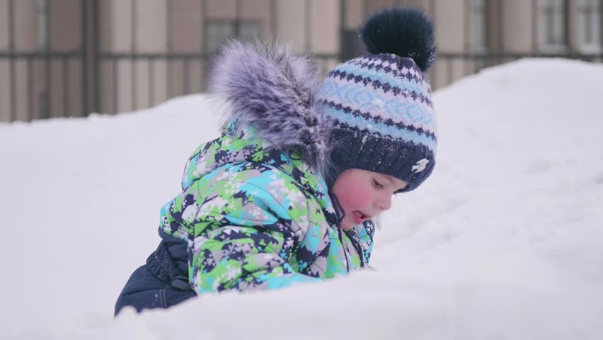 A small child plays on a snowy mountain, throws snow and laughs . Sunny frosty day. Fun and games in the fresh air.