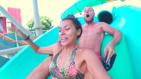 Young Mixed Race Couple Having Fun Riding Down Water Slide Tube and Making Selfie with Gopro Camera. HD Slowmotion.