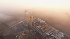 Construction site in the fog with a bird's eye on the Sunset. Aerial Video . Tower crane, excavator and sand. Flying over the construction site. The construction of the plant in the city.