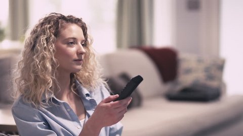 Attractive blonde woman searches through TV channels with nothing to watch