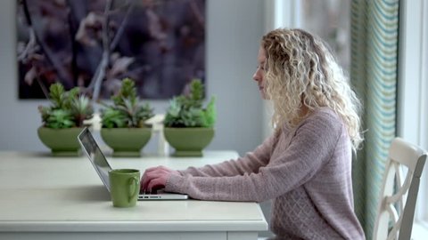 Beautiful blonde woman works on her laptop in a modern home interior