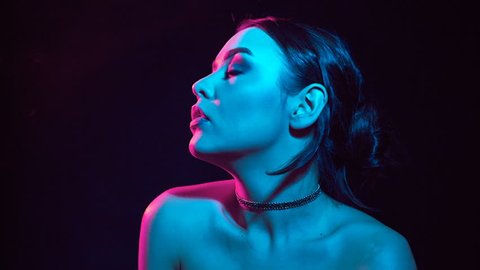 Slow motion portrait of glamour seductive gorgeous brunette woman smoking electronic cigarette in neon color light in studio