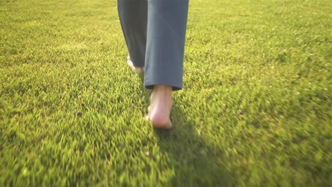 Rea view of an unrecognizable young woman walking on the grass barefoot. Concept of freedom and enjoying one s life. Tracking real time medium shot