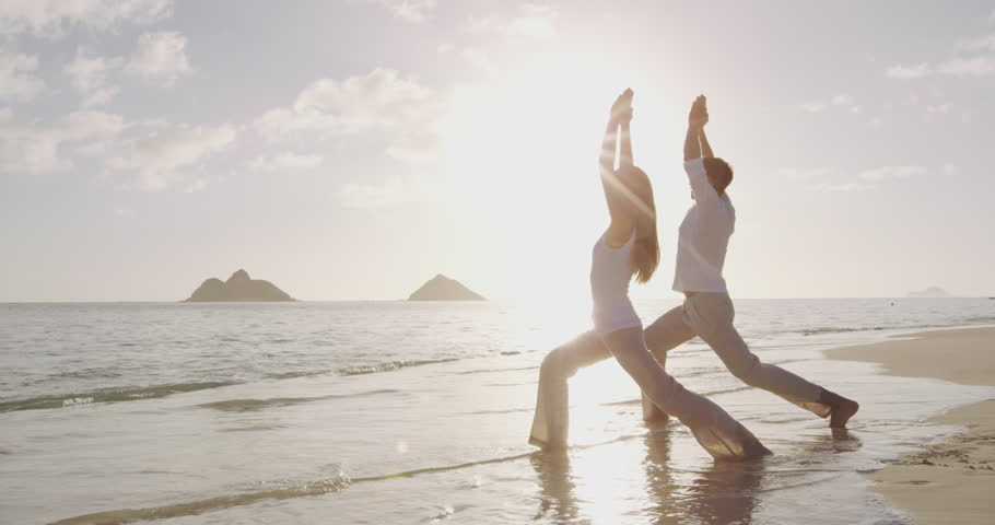Yoga meditation and wellness lifestyle concept. People, man and woman doing yoga exercises on beach at sunrise on beautiful Warrior 1 pose. tion and yoga meditating on beach. | Shutterstock HD Video #1007478847
