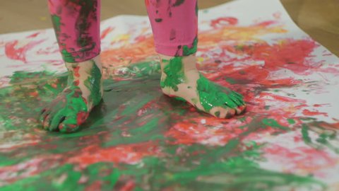 Closeup of a young child's foot gouache stained in paint. The child walks on a large sheet of white paper.