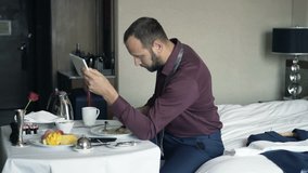 Businessman watching movie on tablet and eating breakfast in hotel room