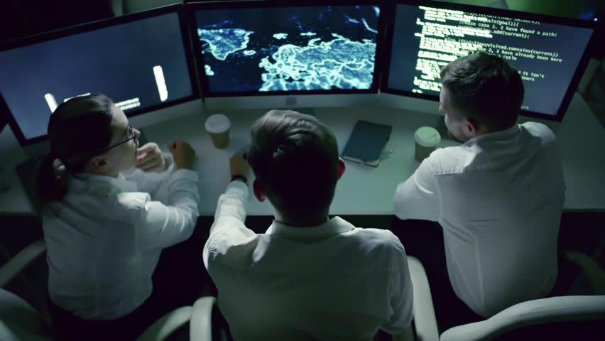 High angle view of professional team of IT security specialists speaking in front of computer monitors in dark office at night; computer code and holographic world map on display Royalty-Free Stock Footage #1007488336