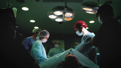 Doctor wearing protective clothing performing surgery using sterilized equipment. Medical Team Performing Surgical Operation in Bright Modern Operating Room