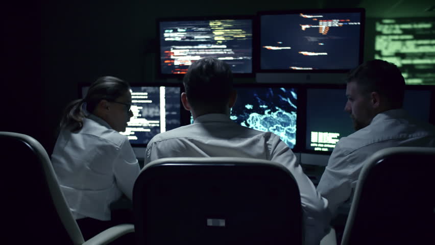 Rear view of three IT specialists discussing cyber security at desk in front of multi-display workstation in dark office at night Royalty-Free Stock Footage #1007490898