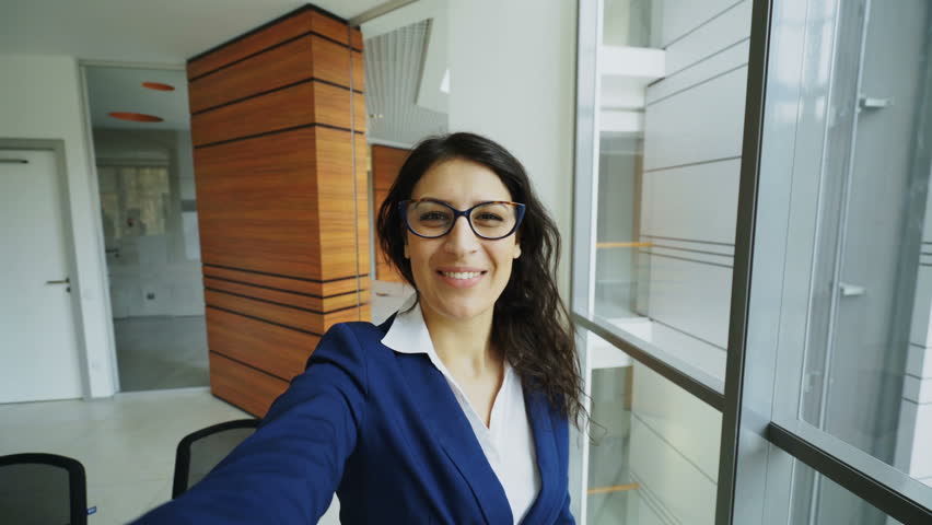 POV of young businesswoman in suit having online video chat using smartphone camera and talking to his colleagues in modern office