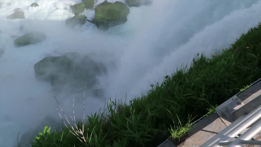 Close up view of American Falls waterfall in Niagara New York starting with view looking down edge of cliff and ending with view across falls towards Canada with thunderous sound of rushing water.