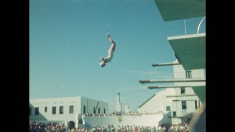 1940s: Woman dives badly, splashes. Crowd watches. Woman runs, jumps off diving board, does somersault. Man dives off high platform. Two women dive in sync. Man dives, twists, off high platform.