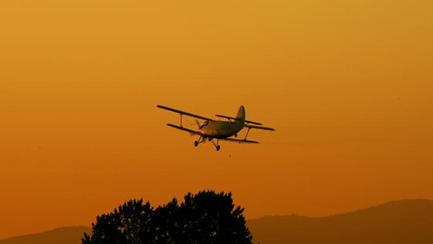 A crop duster applies chemicals to a field at sunset