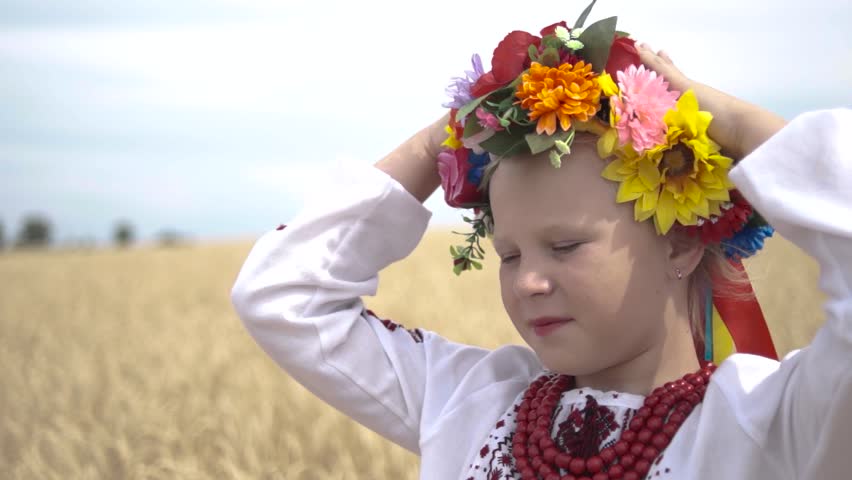 Ukraine. Field with yellow wheat. Girl in a national Ukrainian costume straightens the wreath on her head. Close-up