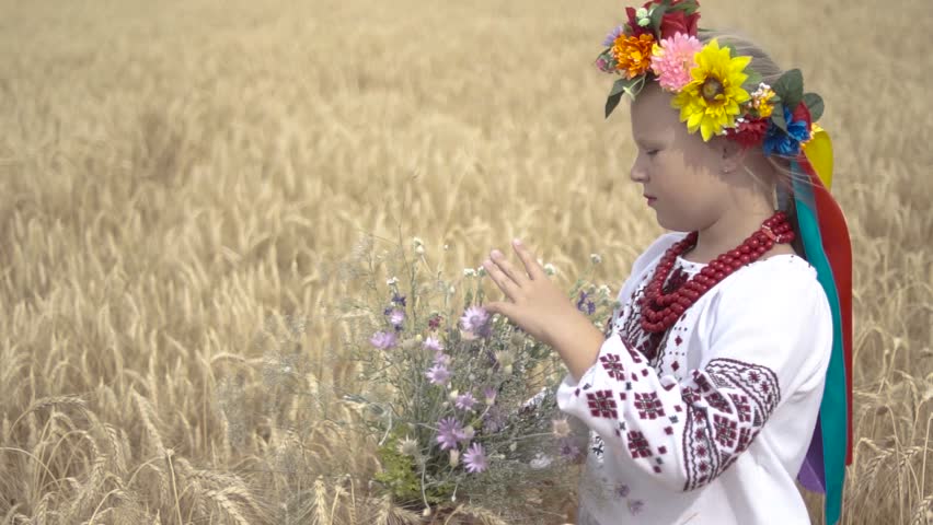 Ukraine. Girl in a national Ukrainian costume holds a bouquet of flowers in a field with yellow wheat