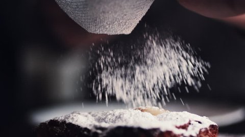 Slow motion shot hands of cook adding powdered sugar on the peice pie as a topping
