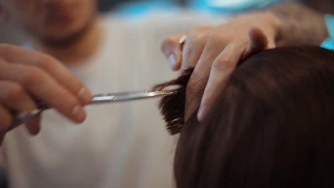 Barbers hands uses scissors for shaping mens hair in a beauty saloon. Video with beautiful bokeh and tone . Soft focus.