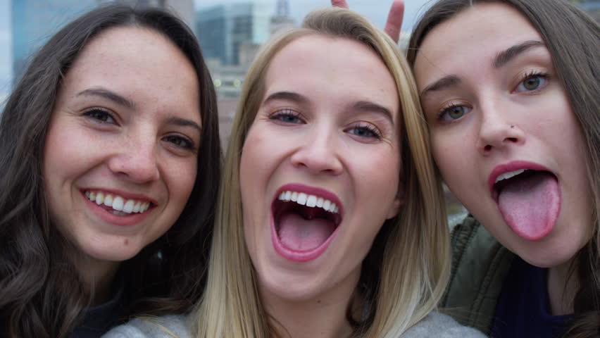 Group Of Carefree Girls Make Funny Faces And Smile For Selfies, City In Bac...