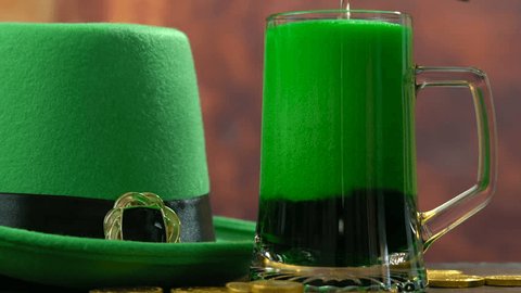 St Patrick's Day pouring green beer with green leprechaun hat and gold coins against rustic background, panning up.