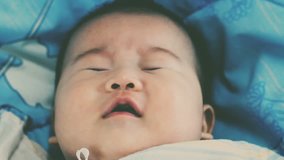 Close up face of a two-month adorable asian baby relaxing. Newborn baby yawning and lying on the bed. Healthy children concept. Vintage film filter effect. Cinematic style colors.