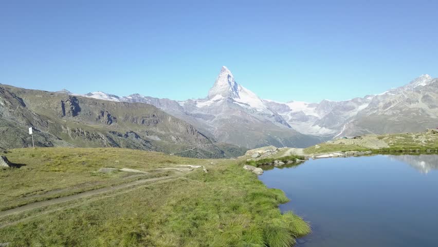 Drone flying aerial view of Matterhorn from Lake Stellisee above Zermatt with the reflection of the mountains in a clear water going further backwards nature Royalty-Free Stock Footage #1007522857