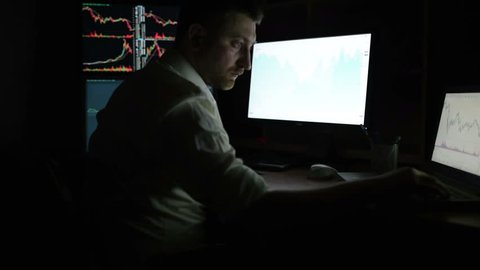 Stockbroker in white shirt is working in a dark monitoring room with display screens. Stock Exchange Trading Forex Finance Graphic Concept. Businessmen trading stocks online.