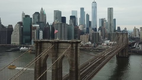 NEW YORK CITY - FEB 2, 2018: Brooklyn Bridge aerial over American flag toward Freedom Tower Manhattan skyline in NYC. The famous suspension bridge is one of the oldest roadway bridges in the US.