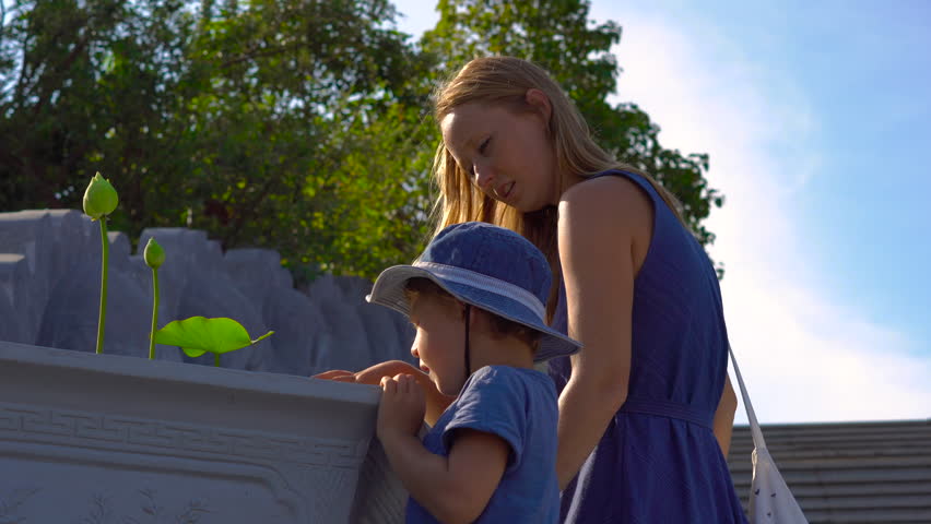 Tourists mother and son looking at a lotus plants in a huge ceramic vessel with water inside of a buddhist temple on Phu quoc island, Vietnam