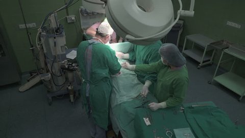 A team of senior surgeons, medical technicians and anesthesiologist using surgical tools and instruments to operating patient in operation theater, wide angle view, crane shot, steady cam, real scene.