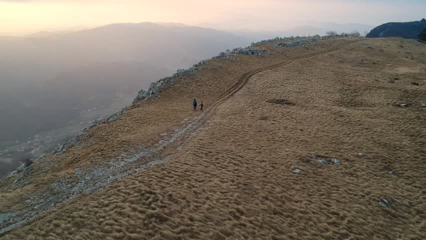 Aerial view of woman and child hiking on the mountain ridge in barren mountain landscape