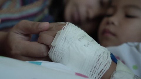 Young mother is holding hand bandaged of little daughter with love and care while they lying on bed in the hospital in slow motion shot