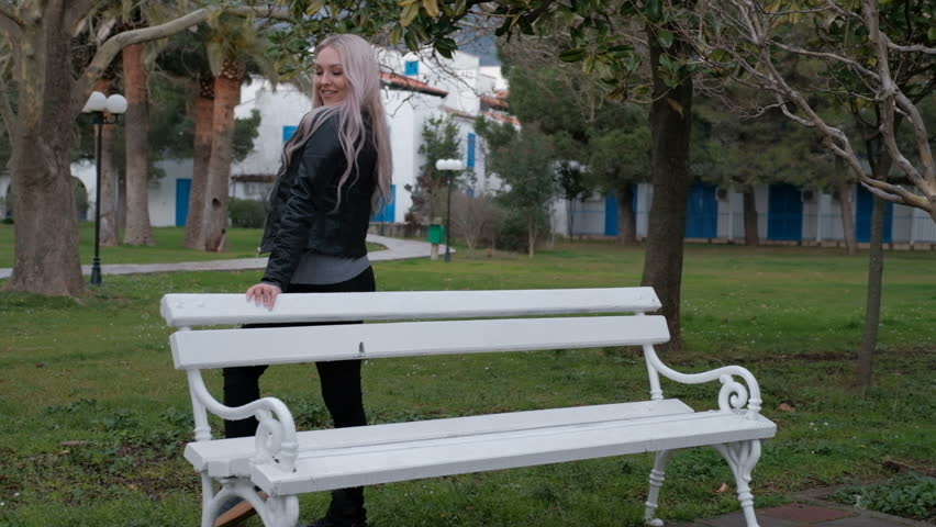 Young attractive woman with long blonde hair  in a leather jacket in the spring walking in park. Slow motion