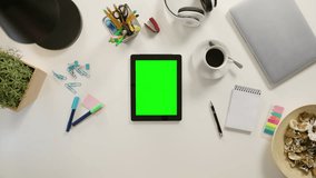 Fingers zooming out on a tablet with a green screen. The tablet is on the white table. View from the top. Close-up.