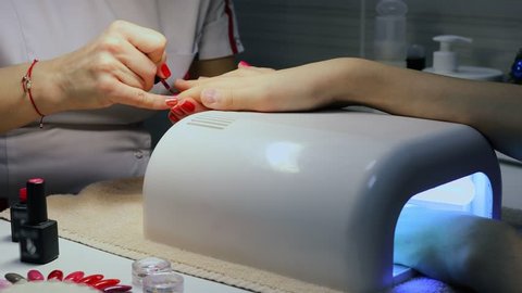 Woman shellacs girls nails on table with dryer in beauty salon