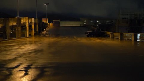 A sad man walks alone through a city parking lot at night