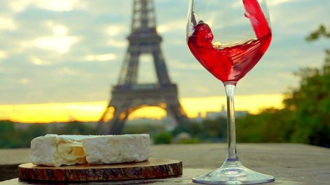 Red wine is poured into a glass. Piece of Camembert cheese with a wooden board. The Eiffel Tower. Sunset