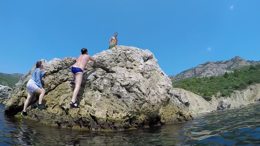 A man with a running start dives into the sea from the cliff. Slow motion.