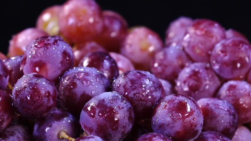 Amazing sprinkling in slow motion, 240fps, of pink and violet grapes close up, rotating to the right on black background. Eco product for healthy food. Excellent vegetarian macro with vibrant texture.
